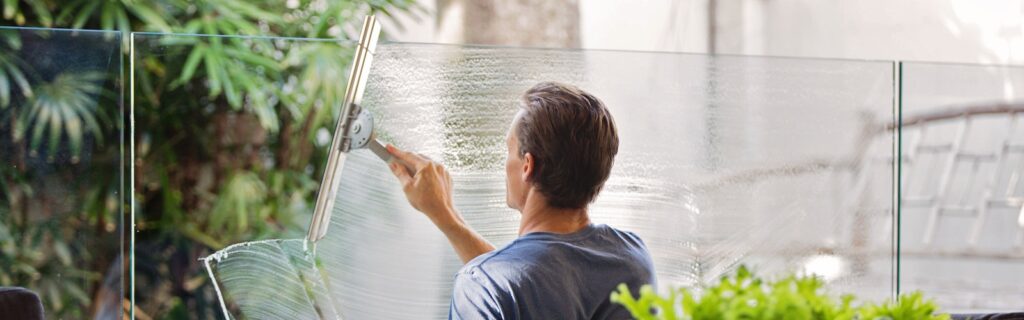 Man in Gray Shirt Cleaning Clear Glass Wall Near Sofa