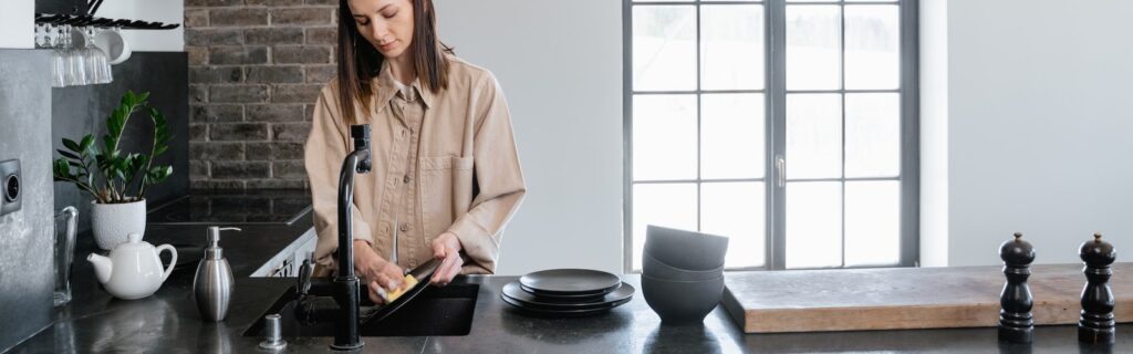 A Woman Standing Near the Kitchen Sink Washing the Dishes